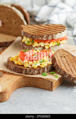 Scrambled eggs and smoked salmon on rye bread with green onions. A sandwich for breakfast. Selective focus Stock Photo