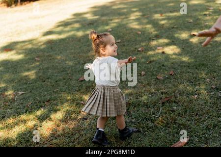 happy toddler girl standing with outstretched hands while playing in park,stock image Stock Photo