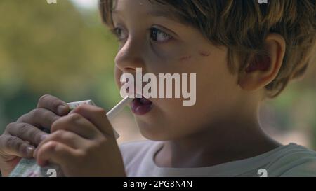 Portrait of a child drinking juice from straw from carton box outside. One little boy snacking outdoors Stock Photo