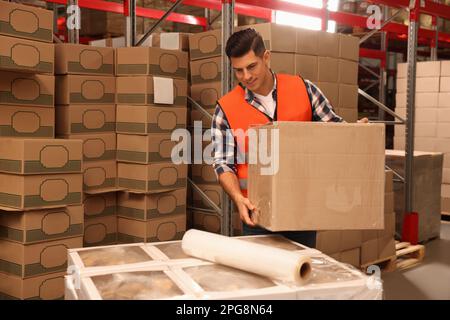 Worker with box wrapped in stretch film at warehouse Stock Photo