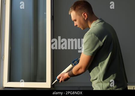 Construction worker sealing window with caulk indoors Stock Photo