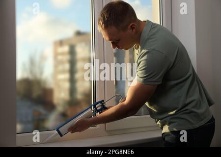 Construction worker sealing window with caulk indoors Stock Photo