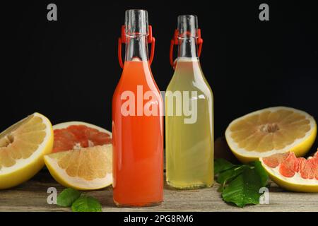 Glass bottles of different pomelo juices and fruits on wooden table against black background Stock Photo