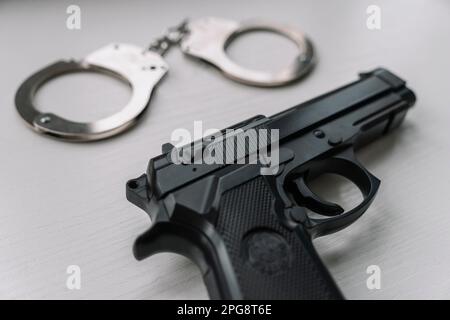 Black handgun gun with handcuffs on wooden surface. Arrest concept. Stock Photo