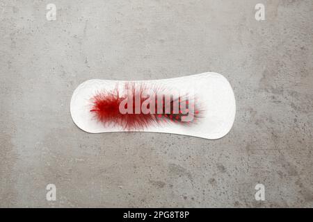 Sanitary pad with red feather on grey background, top view. Menstrual cycle Stock Photo