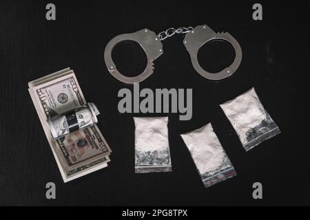 narcotic powder in a bag of money and handcuffs on a black background of the table. The concept of drug trafficking or drug trafficking. Stock Photo