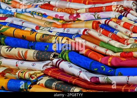 Colourful home decor fabrics printed with bright and vibrant designs stacked for sale on a stall in the regular market in Place Michel Debré, the busy square below the Château Royal d’Amboise, the impressive castle and former residence of the French kings on the south bank of the River Loire at Amboise, Centre-Val de Loire, France. Stock Photo