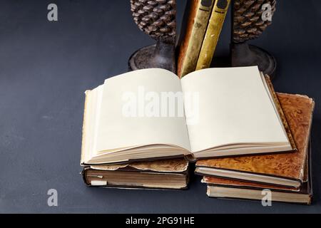 Shabby vintage book with blank pages in stack of books and book holder on black concrete table. Open notepad with blank pages with copy space Stock Photo