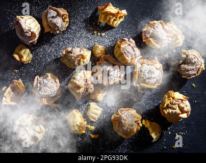 Yellow mini walnut tarts dusted with powdered sugar on a dark gray anthracite stone background Stock Photo