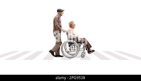 Full length profile shot of an elderly man pushing an elderly woman in a wheelchair at a pedestrian crossing isolated on white background Stock Photo
