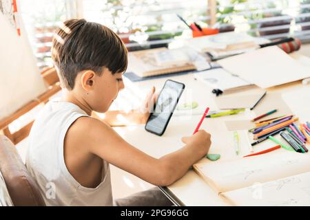 A boy is learning to draw with her smart phone. Online education. Concept of technology and learning. Stock Photo