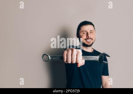 Smiling happy bearded man holding wrench in one hand. Focus in the foreground. Illustrating industrial themes, occupation, and industry Stock Photo