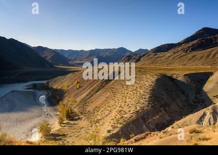 Mountain terraces near the Katun River with wires of power lines near the road in autumn in Altai in Siberia during the day. Stock Photo