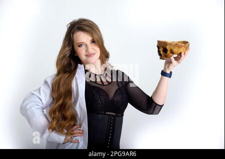 attractive holds a skull in her hands concept of photography is suitable in the field of cosmology, medicine and healthcare Woman in a white robe and black evening dress beautiful bright fierce Stock Photo