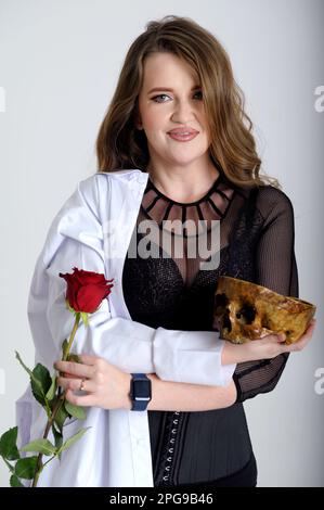 attractive holds a skull in her hands concept of photography is suitable in the field of cosmology medicine and healthcare in the hands of a woman with a medical gown rose choice between life and work Stock Photo