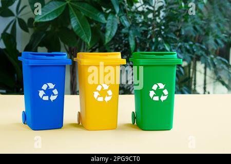 Blue, yellow and green tank for separate garbage collection against bacground with green plants, waste recycling and conservation of the environment c Stock Photo