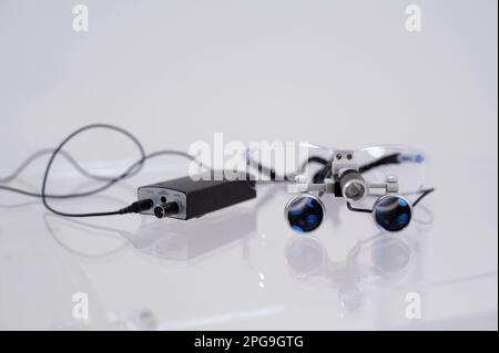 binoculars close-up on a white table dental appliances for treatment of gums teeth prosthetics filling canals magnification of the image for surgeon to work with instruments in surgical operations Stock Photo