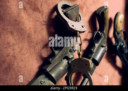 A pair of black handcuffs on top of a black retro pistol. Stock Photo