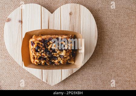 Raisin Walnut cinnamon roll close up on a wooden heart-shaped board, flat lay with copy space Stock Photo