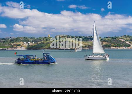 Lisbon, Portugal day view of Tagus river with passengers aboard a modern hop-on hop-off cruise boat next to a sailing yacht. Stock Photo