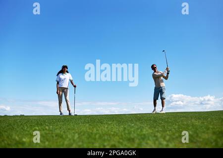 Full length portrait of active sporty couple playing golf on field against blue sky, copy space Stock Photo