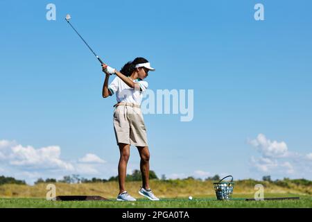 Side view portrait of sporty woman playing golf on green grass outdoors and swinging golf club, copy space Stock Photo