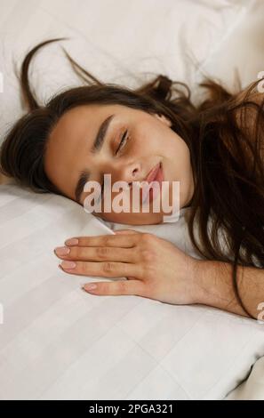 Portrait of a beautiful young woman who sleeps sweetly on the bed. Lying on a soft pillow close-up. Vertical frame. Stock Photo