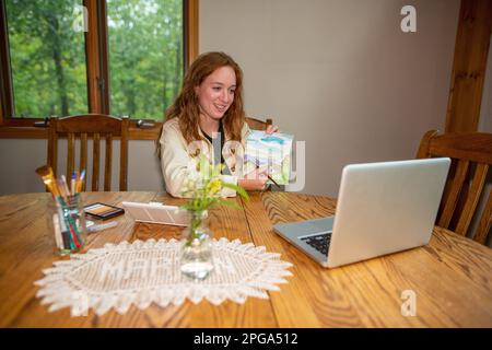 A young teacher holding a drawing she just made and explaining a complicated technique to her students during an online lesson Stock Photo