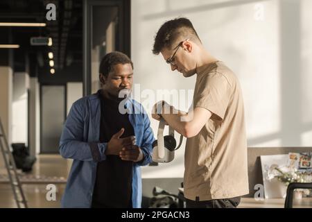 Colleague helps put on vr headset. Testing metaverse world, touching virtual reality subjects. IT Development Team Working on VR Project. Abstract Stock Photo