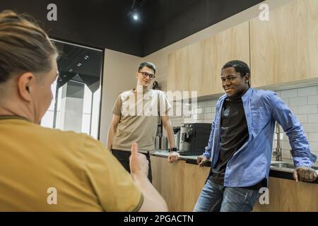 Group of cheerful young people talking and smiling during coffee break time in the office. Team of professional software developer relaxing in the Stock Photo
