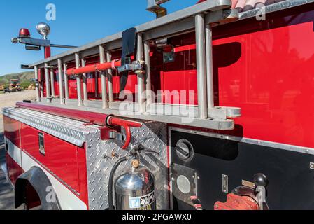 Beaching fire pick ax and sturdy extension ladder is firmly secured to the side of the red fire truck. Stock Photo
