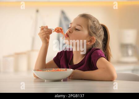 Cute little girl eating tasty pasta at table in kitchen Stock Photo