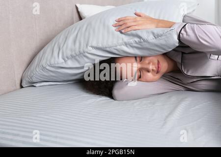 African American woman covering head with pillow in bed at home Stock Photo