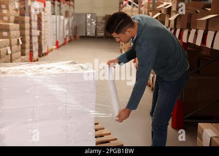 Worker wrapping boxes in stretch film at warehouse Stock Photo