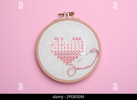 Canvas with embroidered heart and needle in hoop on pink background, top view Stock Photo