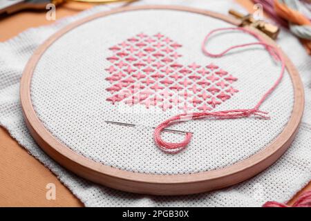 Canvas with embroidered heart and needle in hoop on orange background, closeup Stock Photo