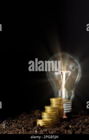 rising piles of coins with lighted light bulb on black background ...