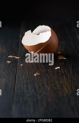 brown egg shell broken or crack with pieces scattered on the surface, isolated on rustic black table top surface with blurry background Stock Photo