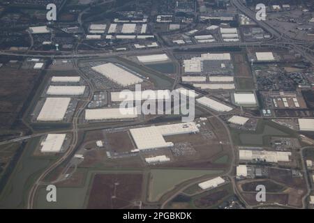 From above, the sprawling industrial warehouse complex stretches as far as the eye can see, with rows of metal roofs and loading docks. Stock Photo