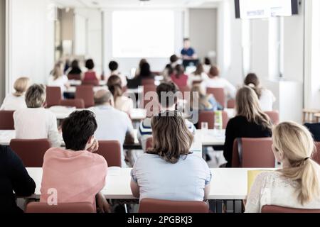 Speaker giving presentation in lecture hall at university. Participants listening to lecture and making notes. Stock Photo