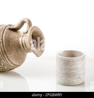 An earthenware jug for wine lying on its side and a glass with reflection in the glass background. Stock Photo