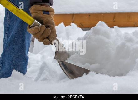 Close up view of an unrecognizable adult person shoveling deep snow on a residential deck on a sunny winter day Stock Photo