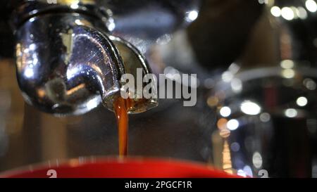 isolated macro close up of an espresso coffee shot pouring from a signgle portafilter handle into a bright red cup. Barista made coffee detail. Stock Photo