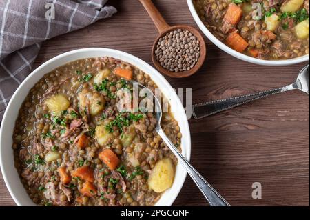 Lentil stew with potatoes, vegetables and smoked pork meat on a plate on wooden table from above Stock Photo