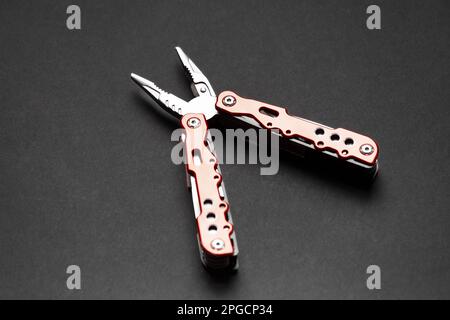 universal multifunctional knife pliers with different nozzles and a red handle on a dark gray background. Versatile camping knife. Stock Photo