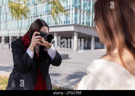 Anonymous young female photographer taking picture of woman with photo camera while standing on street Stock Photo