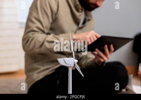 Unrecognizable bearded male engineer in casual clothes browsing tablet while sitting on floor near windmill layout Stock Photo