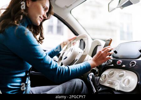 Side view of female driver using navigator in smartphone while driving modern car with white steering wheel Stock Photo