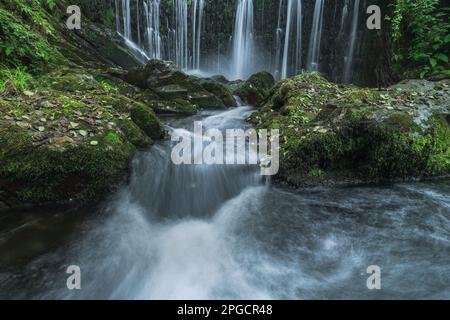 Picturesque scenery of waterfall flowing through rough rocky mountains covered with green moss in forest Stock Photo