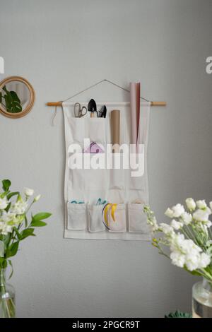 White organizer with pockets and floral equipment hanging on wall near bouquets of fresh flowers in vases Stock Photo